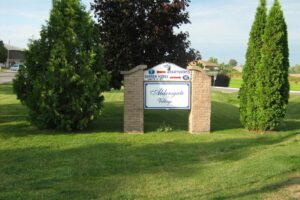 two brick pillars with aldersgate front entrance sign in the middle with red arrow pointing left for apartments and a red arrow pointing right for garden homes. Surrounded by green grass and mature trees and hedges.