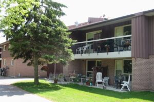 Aldersgate two story apartment building with balcony surrounded by green grass and mature pine tree