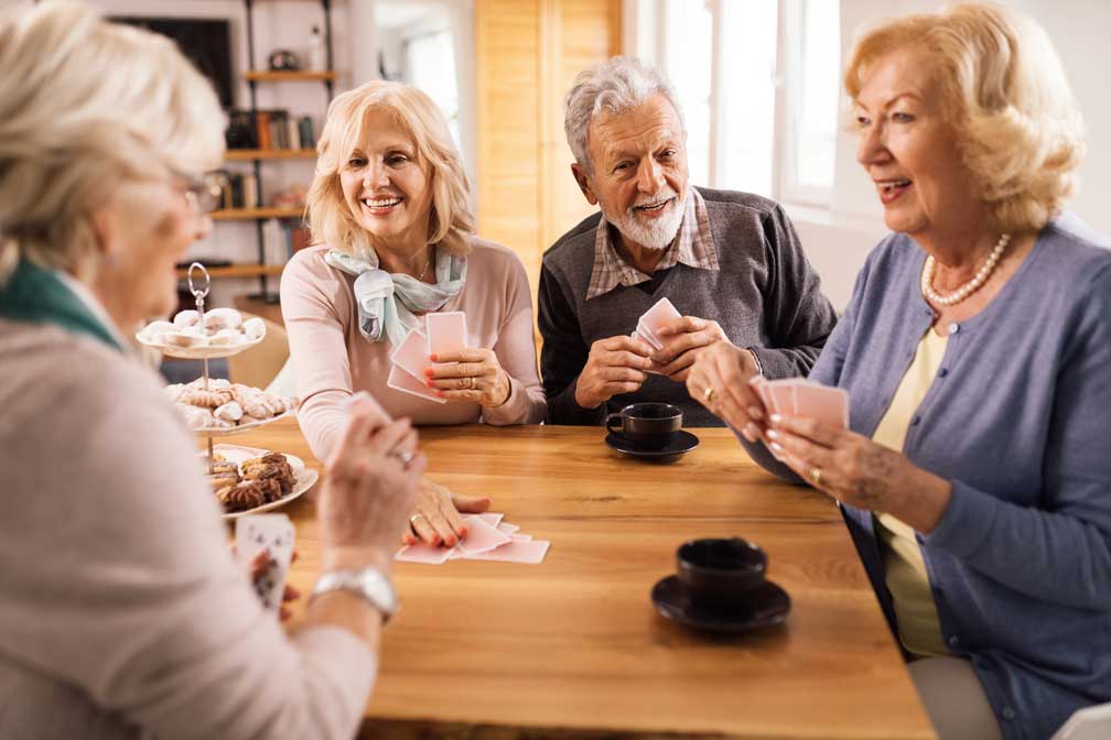 a group of happy seniors playing a card game at a table with coffee and tiered tray of sweets